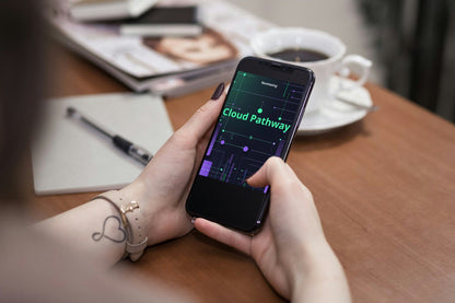 Person holding a smartphone with 'Cloud Pathway' app on a desk with coffee and notebook.