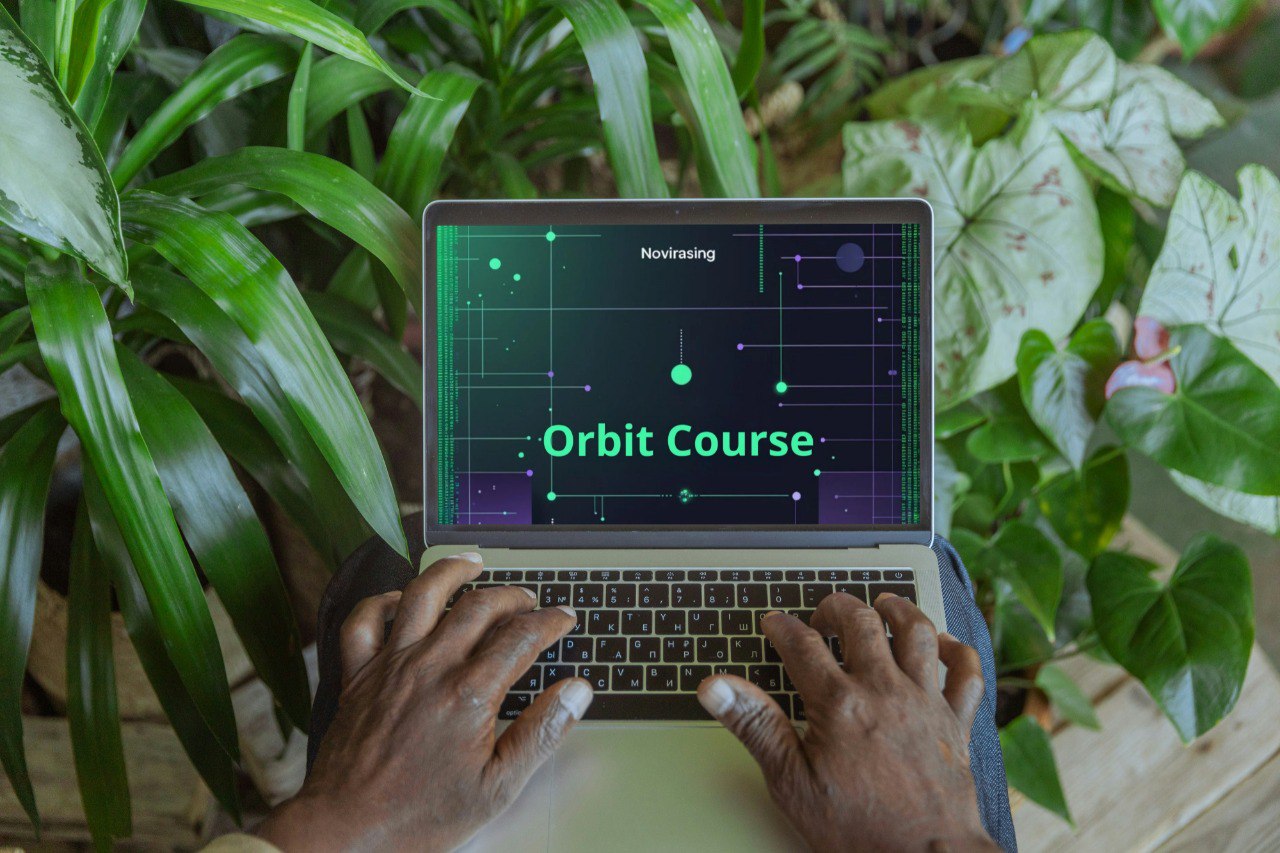 Person using a laptop with 'Orbit Course' displayed on the screen, surrounded by green plants.