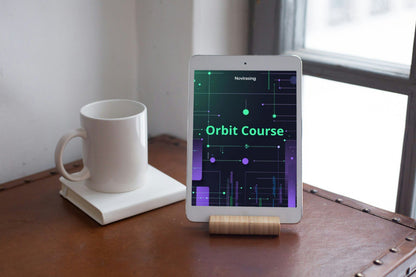 Tablet on a stand displaying 'Orbit Course' app next to a white mug on a wooden surface.