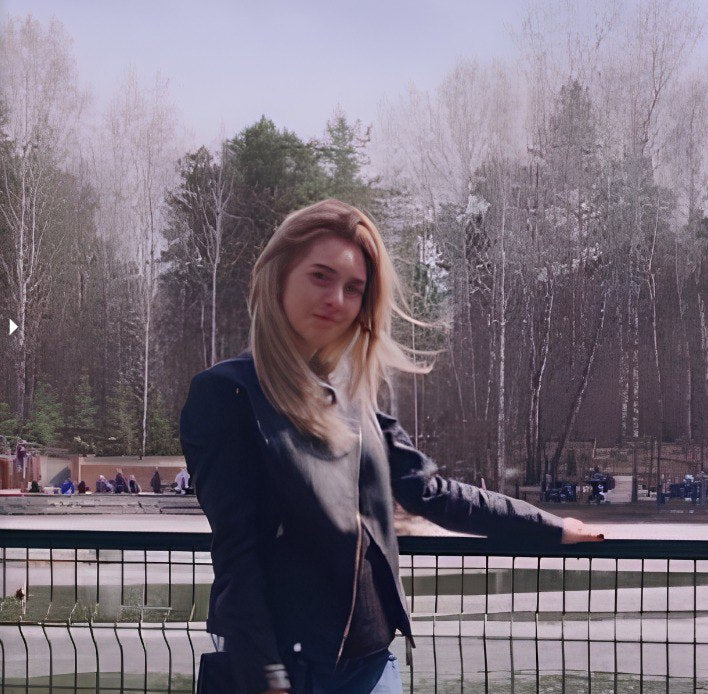 Woman standing by a fence with trees and people in the background